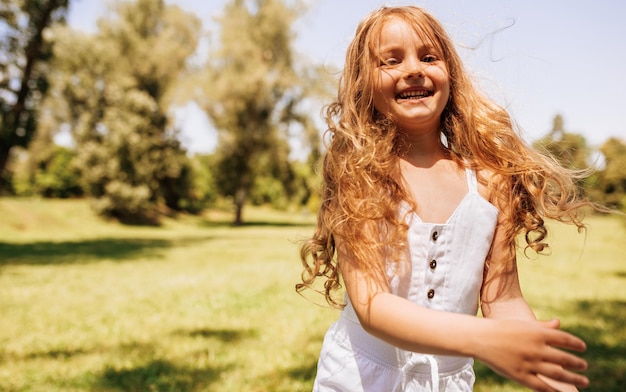 Portret van gelukkig klein meisje met lang blond haar spelen op de achtergrond van de natuur Positief kind genieten van zomerdag in het park Vrolijk kind plezier in het bos op zonlicht Gelukkige jeugd