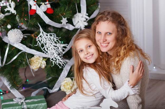 Portret van gelukkig lachend meisje met moeder zitten in de buurt van de kerstboom