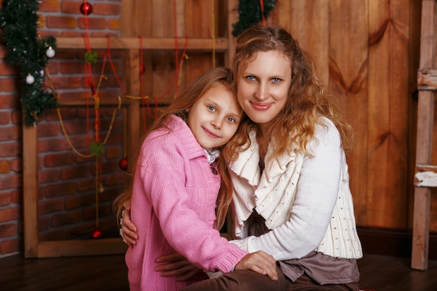 Portret van gelukkig lachend meisje met moeder zittend onder kerstversiering