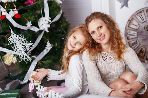 Portret van gelukkig lachend meisje met moeder zittend onder kerstversiering