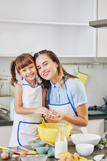 Portret van gelukkig lachend mooie vrouw en haar dochtertje knuffelen en camera kijken na het maken van deeg