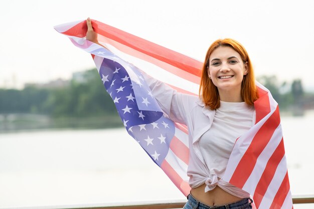 Portret van gelukkig lachend roodharig meisje met de nationale vlag van de VS in haar handen