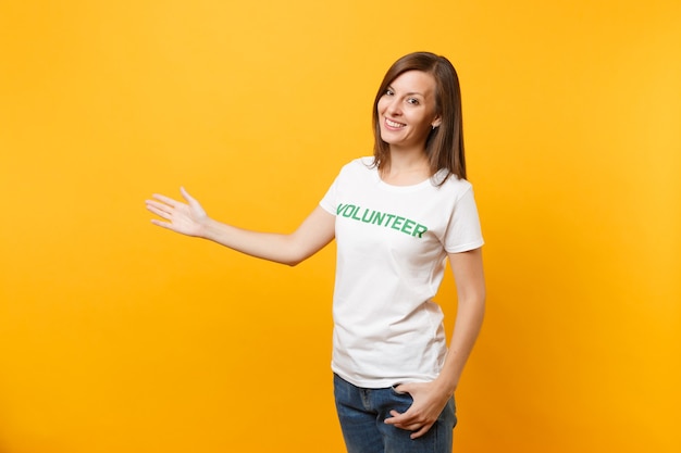 Portret van gelukkig lachende tevreden vrouw in wit t-shirt met geschreven inscriptie groene titel vrijwilliger geïsoleerd op gele achtergrond. Vrijwillige gratis hulp, liefdadigheidswerkconcept.