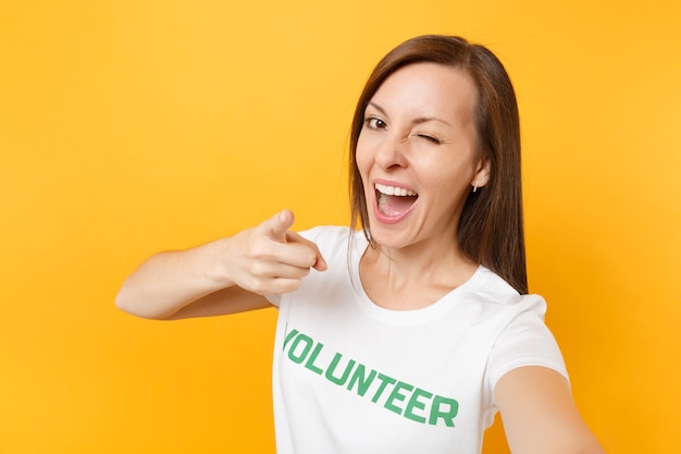 Portret van gelukkig lachende tevreden vrouw in wit t-shirt met geschreven inscriptie groene titel vrijwilliger geïsoleerd op gele achtergrond. Vrijwillige gratis hulp, liefdadigheidswerkconcept.