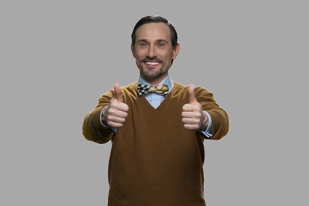 Portret van gelukkig man gebaren duimen omhoog. Vrolijke man op grijze achtergrond. Groot succesconcept.