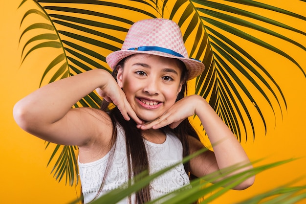 Portret van gelukkig meisje met hoed en palmbladeren op gele achtergrond.