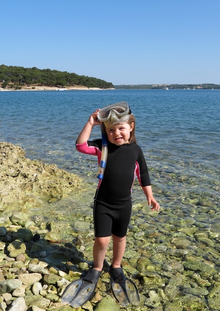 Portret van gelukkig meisje met wetsuit, maskers en snorkels aan zee