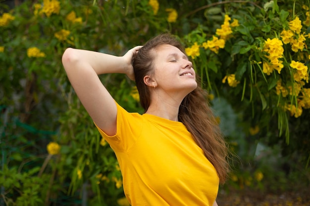 Portret van gelukkig mooi bebaard meisje jonge positieve vrouw met baard ruikt mooie gele bloemen in de tuin glimlachend genietend van lente- of zomerdag diep diep frisse lucht inademen