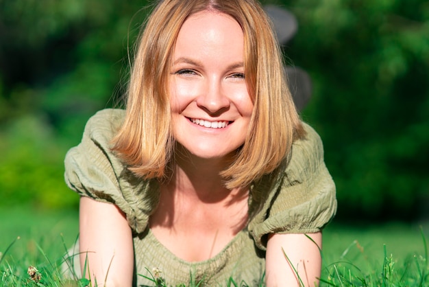 Portret van gelukkig mooi vrij vrolijk meisje, jonge positieve rode kop gember vrouw liggend op het gras in zomer zonnig park in jurk, camera kijken, glimlachend. Jeugd, geluk concept.