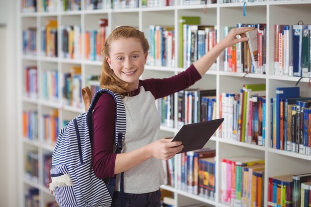 Portret van gelukkig schoolmeisje die boek in bibliotheek selecteren