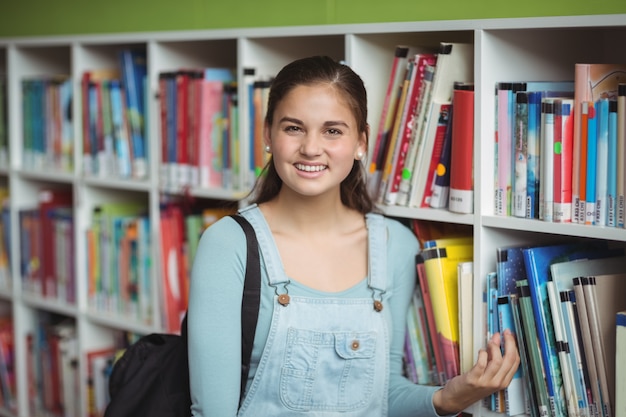 Portret van gelukkig schoolmeisje die boek in bibliotheek selecteren