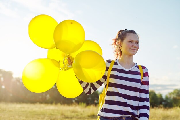 Foto portret van gelukkig tienermeisje 15 jaar oud met gele ballonnen. hemel in wolken, aardachtergrond. vakantie, natuur, tieners, vreugdeconcept