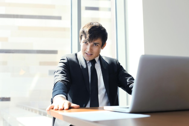 Portret van gelukkig zakenman zittend aan een bureau, kijkend naar camera, glimlachend.