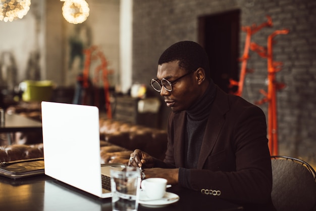 Portret van gelukkige Afrikaanse zakenman die aan laptop in een restaurant werkt.