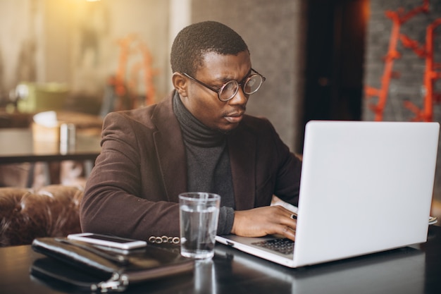 Portret van gelukkige Afrikaanse zakenman die telefoon met behulp van terwijl het werken aan laptop in een restaurant.