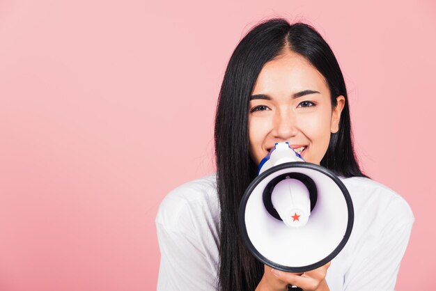 Portret van gelukkige Aziatische mooie jonge vrouw tiener zelfverzekerd lachend gezicht bedrijf aankondiging bericht schreeuwen schreeuwen in megafoon, studio opname geïsoleerd op roze achtergrond, met kopie ruimte