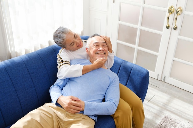 Portret van gelukkige Aziatische senior paar samenwonen knuffel aanraken en omhelzen met een glimlach op de bank in de woonkamer Pensioen samenwonen thuis