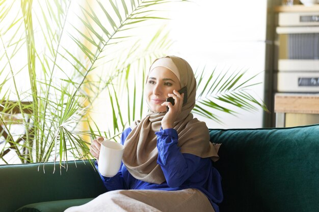 Portret van gelukkige aziatische vrouw die hijab draagt die met mobiele telefoon belt
