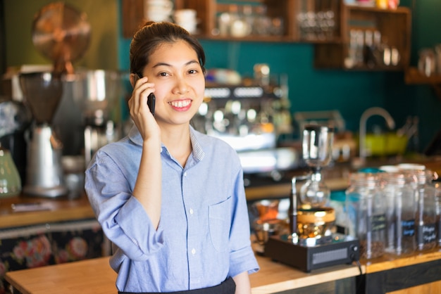 Portret van gelukkige Aziatische vrouwelijke barista die orde neemt via mobiele telefoon