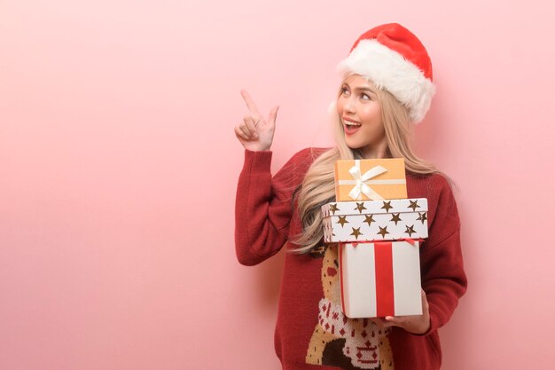 Portret van gelukkige blanke jonge vrouw in kerstman hoed met geschenkdoos over roze achtergrond