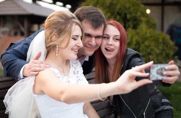 Portret van gelukkige bruid en bruidegom die selfie maken met gast op trouwdag