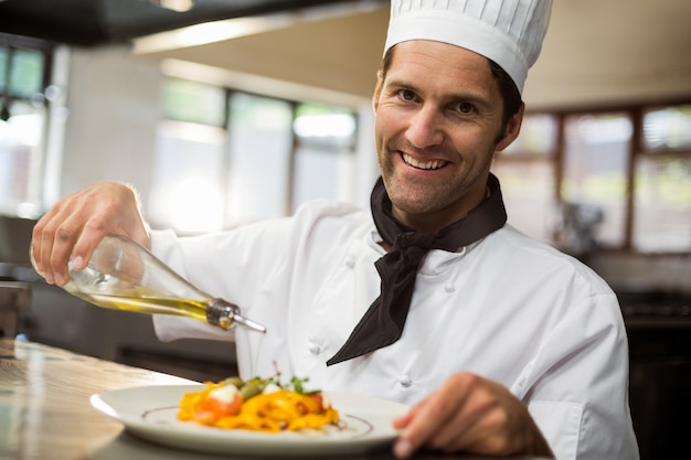 Foto portret van gelukkige chef-kok gietende olijfolie op maaltijd