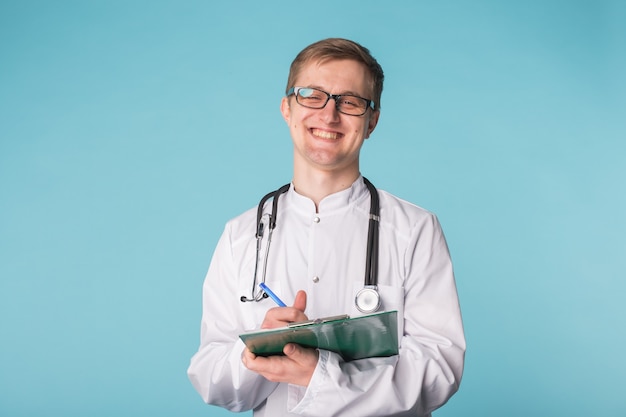 Foto portret van gelukkige dokter die op klembord schrijft tegen een blauwe achtergrond