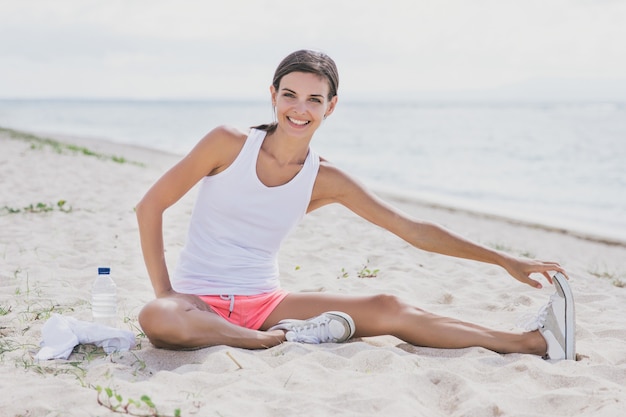 Portret van gelukkige gezonde vrouw die lacht terwijl het doen van been uitrekken op het strand