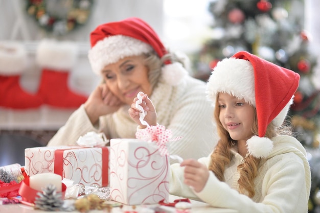 Portret van gelukkige grootmoeder en haar kleine kleindochter die zich thuis samen voorbereiden op Kerstmis