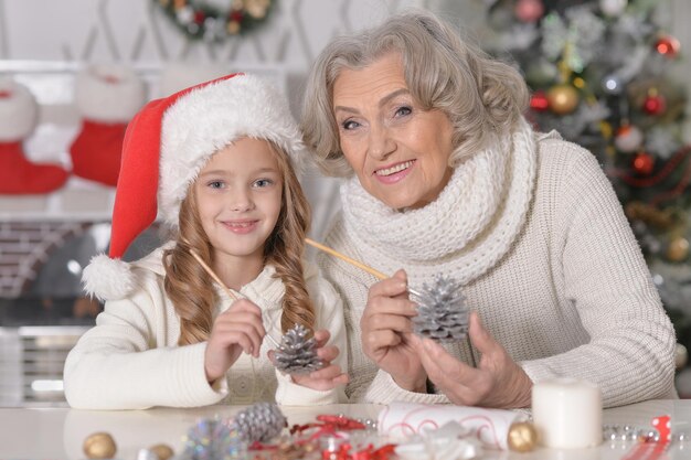 Portret van gelukkige grootmoeder en haar kleine kleindochter die zich thuis samen voorbereiden op Kerstmis