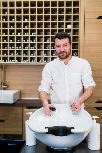 Portret van gelukkige herenkapper met waterkraan dichtbij gootsteen bij salonkapperszaak