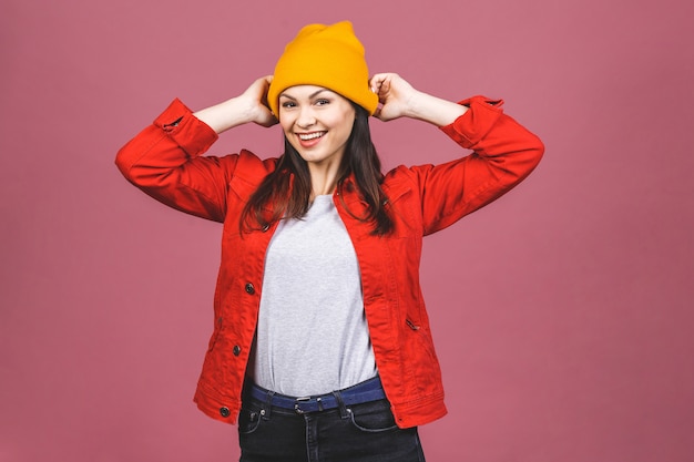 Portret van gelukkige hipster vrouw in gele hoed en rood shirt geïsoleerd over roze muur.