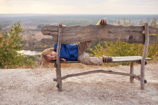 Portret van gelukkige jonge 6 jaar oude jongenszitting op een houten bank buiten