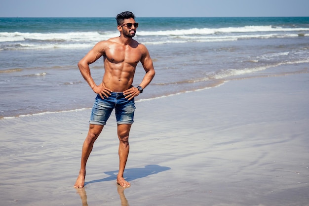 Portret van gelukkige jonge afrikaanse man op het strand. knappe en zelfverzekerde mannelijke harde fitness model mannelijk lichaam bodybuilder met zes pack. india trainer met perfecte buikspieren, schouders, biceps, triceps, borst