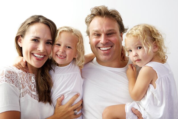 Foto portret van gelukkige jonge familie die samen tegen witte achtergrond glimlacht