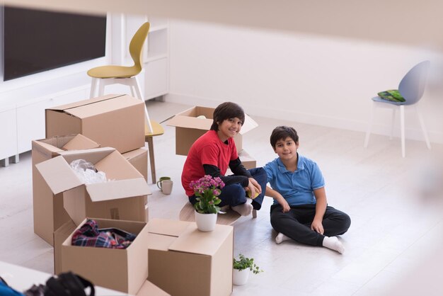 portret van gelukkige jonge jongens met kartonnen dozen om hen heen in een nieuw, modern huis