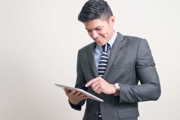 Portret van gelukkige jonge knappe Aziatische zakenman die digitale tablet met behulp van