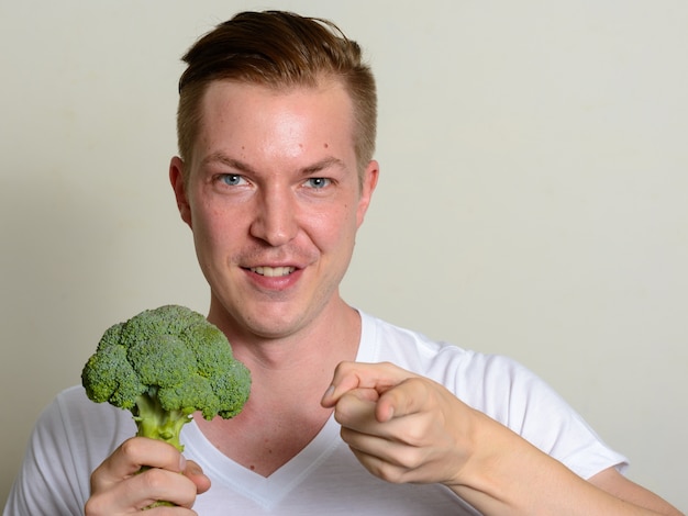 Portret van gelukkige jonge knappe man met broccoli en wijzend op camera