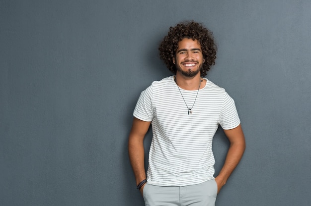 Portret van gelukkige jonge man met krullend haar staande tegen een grijze achtergrond