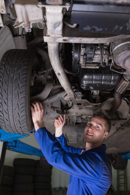 Portret van gelukkige jonge mannelijke werktuigkundige die onder auto werken