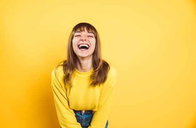 Portret van gelukkige jonge vrouw die bij camera glimlacht die op heldere gele achtergrond wordt geïsoleerd