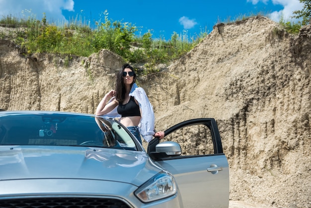 Portret van gelukkige jonge vrouw in de buurt van auto in de zomertijd van het zandstrand om te ontspannen