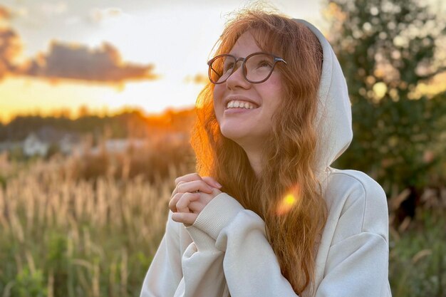 Portret van gelukkige jonge vrouw in glazen bij zonsondergang op natuurlijke achtergrond glimlach en camera kijken