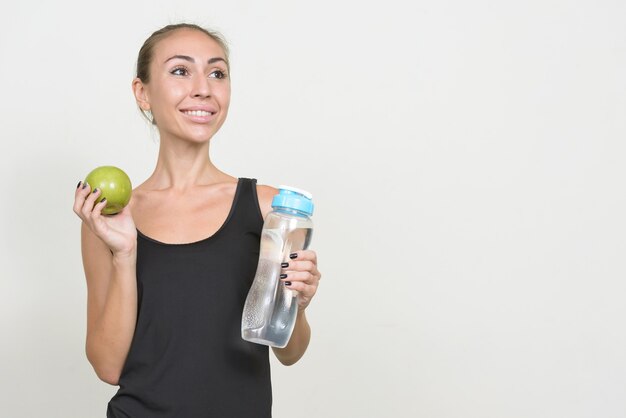 Portret van gelukkige jonge vrouw met appel en waterfles die klaar voor gymnastiek denken