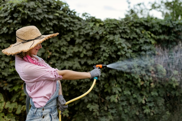 Portret van gelukkige jonge vrouwentuinman die tuin met slanghobbyconcept water geeft