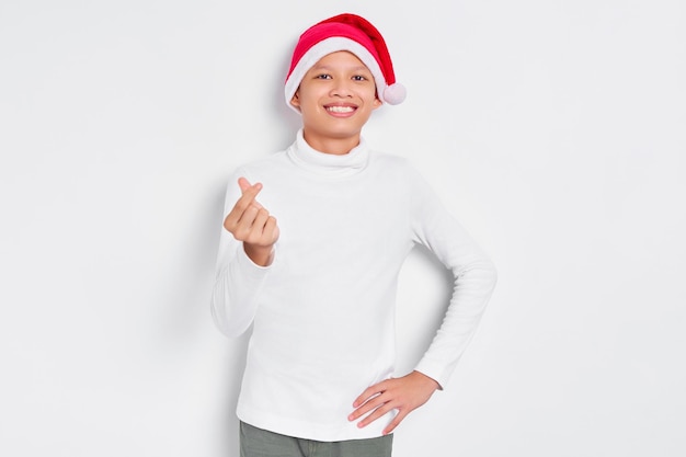 Portret van gelukkige kleine Aziatische man in kerstmuts weergegeven: hart teken met vingers gekruist geïsoleerd op witte achtergrond Gelukkig Nieuwjaar 2023 vakantie concept