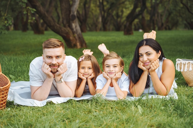 Portret van gelukkige lachende jonge ouders en twee kinderen die samen op een picknickkleed op een zonnige dag liggen. Liefde, familie en een gelukkig levensstijlconcept uit de kindertijd