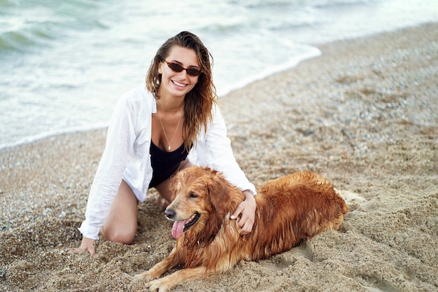 Portret van gelukkige leuke jonge vrouw die en haar hond op het strand zitten koesteren