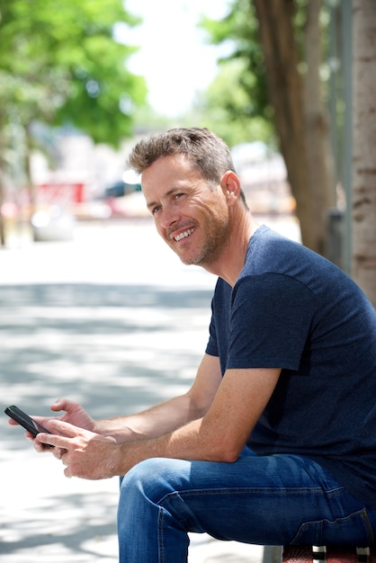 Portret van gelukkige man zittend op een bankje met mobiele telefoon