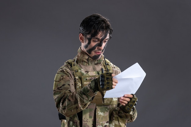 Portret van gelukkige mannelijke soldaat in camouflage leesbrief op donkere muur